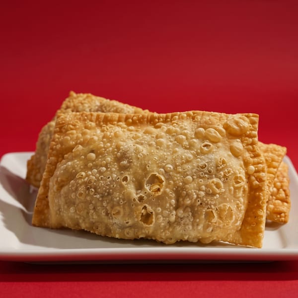 Crispy golden-brown Brazilian pastéis, savory pastries, on a white plate against a vibrant red background.